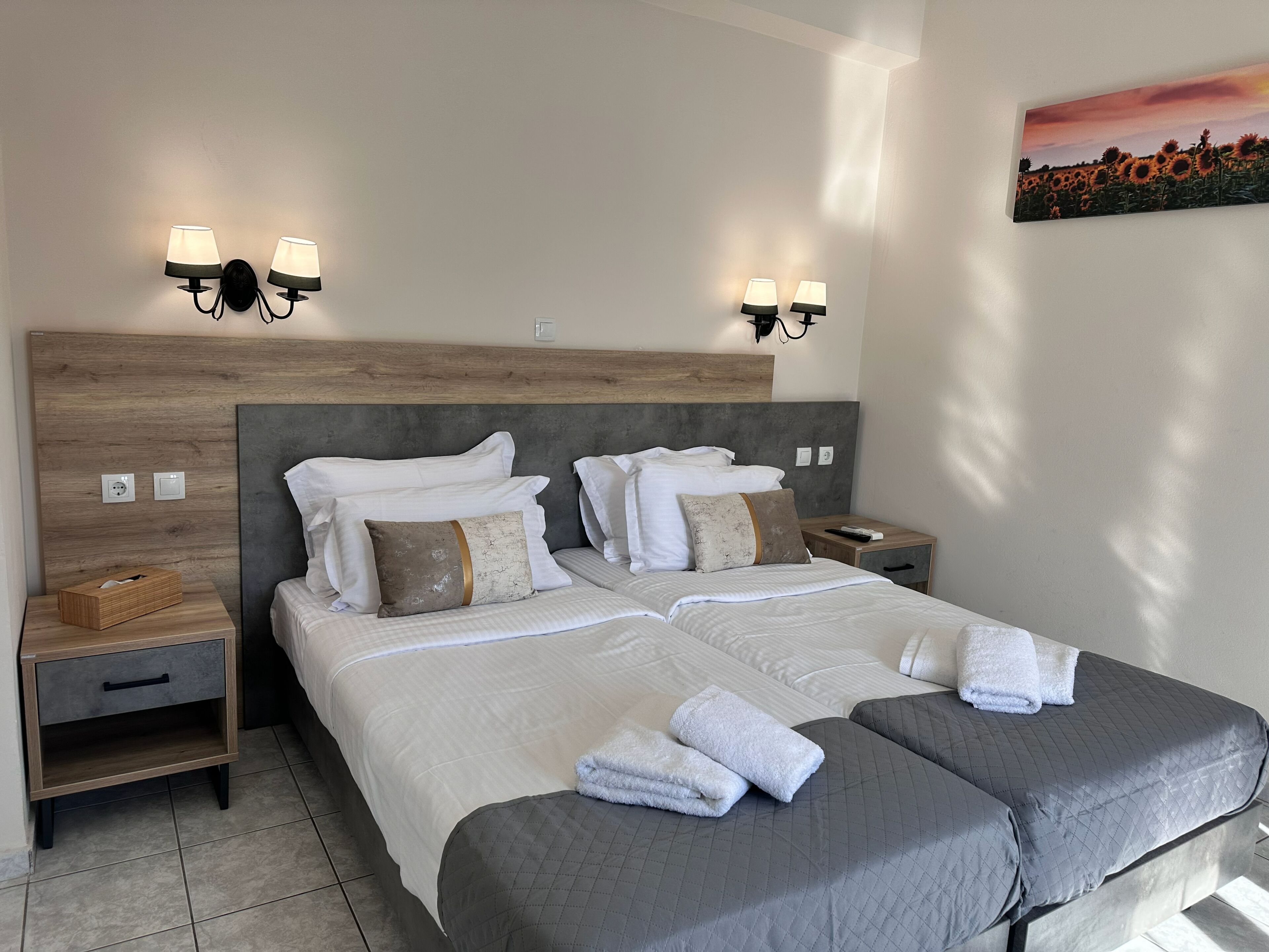 Un lit double avec du linge de lit blanc, deux tables de chevet avec des lampes, une petite table et un tableau au mur.