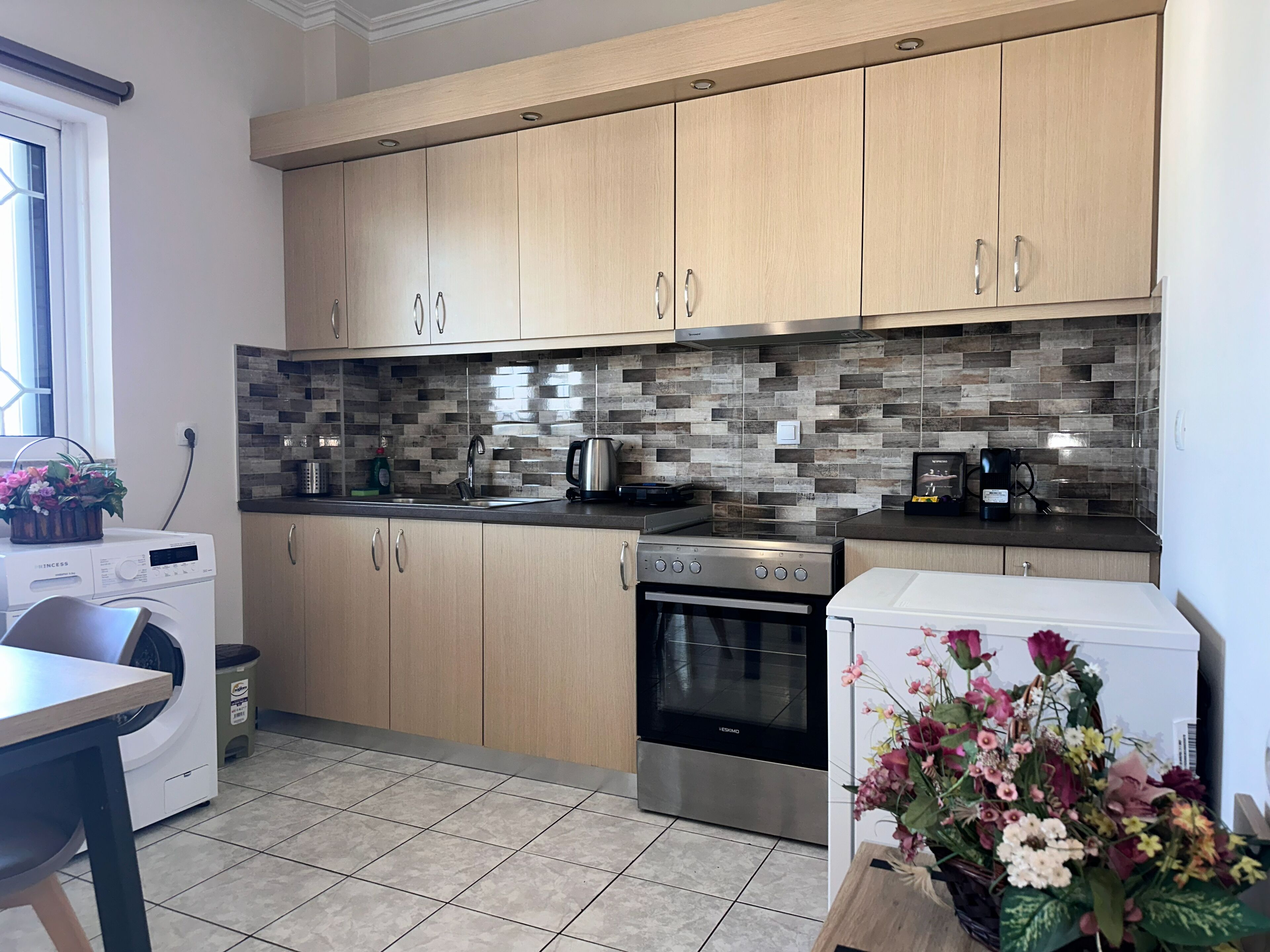 A modern kitchen with wooden cabinets, a tiled backsplash, a stainless steel oven, and a washing machine.