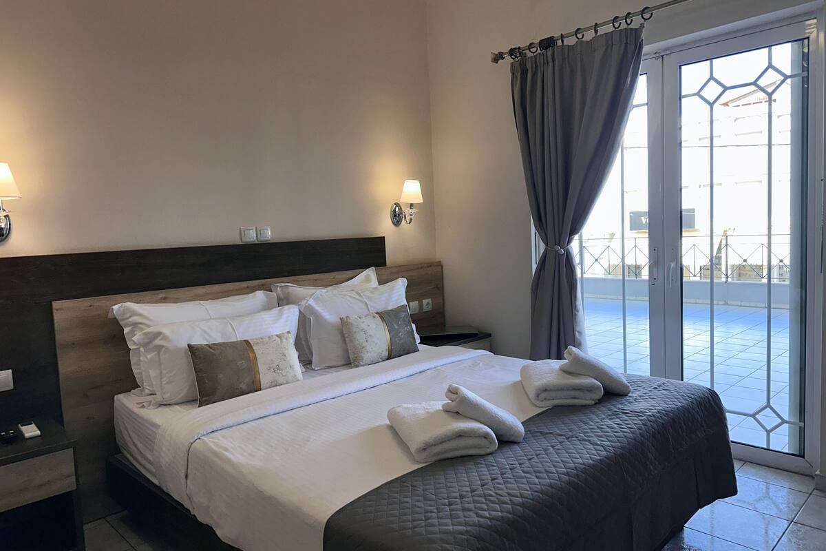Ein Hotelzimmer mit einem großen Bett, zwei Nachttischen, einer Kopfteil und Blick durch eine Glastür hinaus.