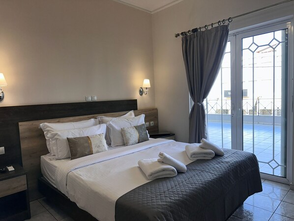 Une chambre d’hôtel avec un grand lit, deux tables de chevet, une tête de lit et une vue sur l’extérieur grâce à une porte vitrée.