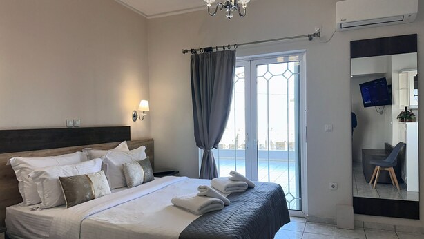 A hotel room with a bed, a chandelier, an air conditioner, a TV, and a view of the outside. - Airport Suites Michelle (Spata-Artemida)