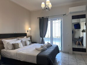 A hotel room with a bed, a chandelier, an air conditioner, a TV, and a view of the outside. - Airport Suites Michelle (Spata-Artemida)