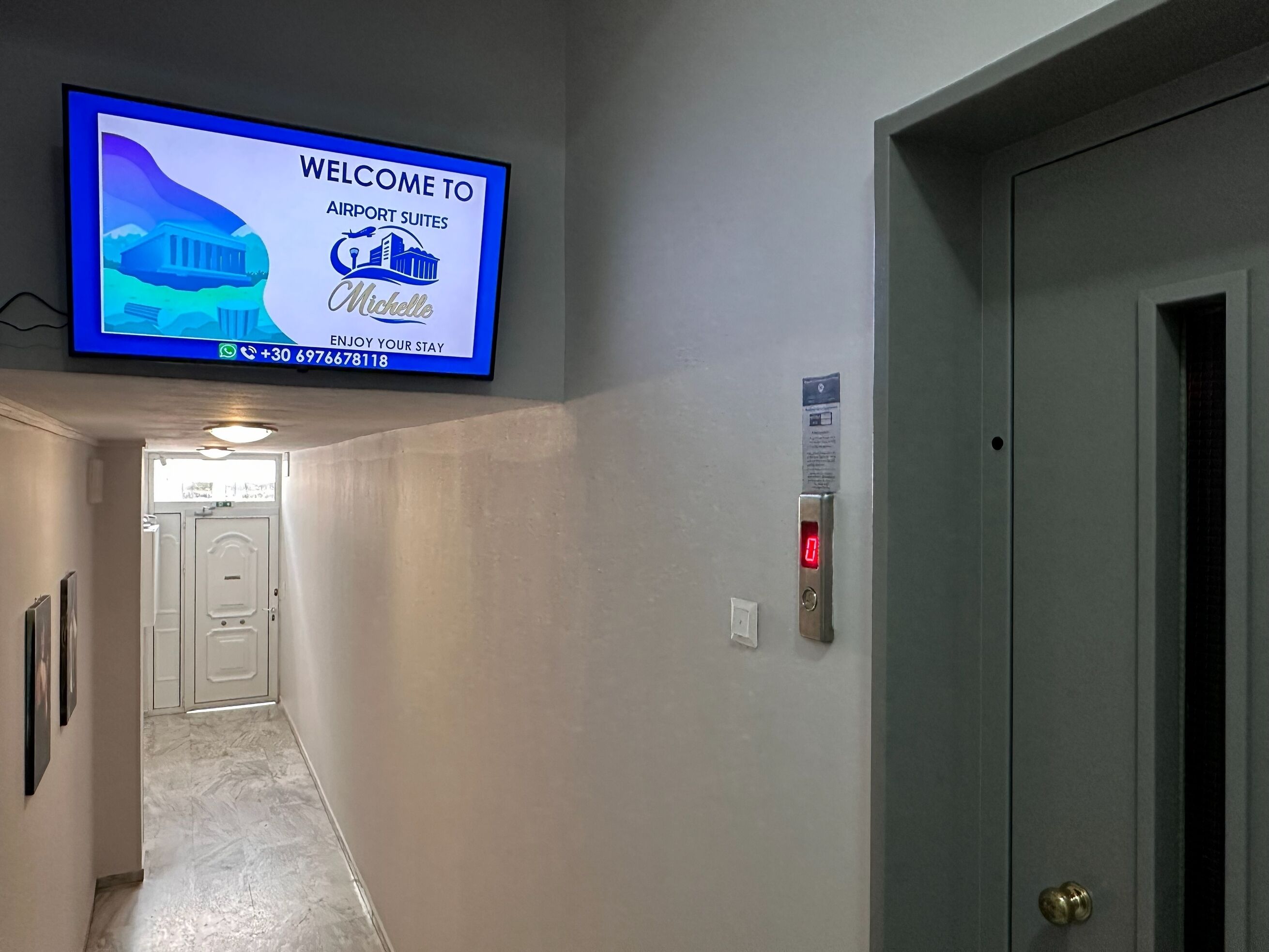 A hotel corridor with a welcome screen, a door, and an elevator.