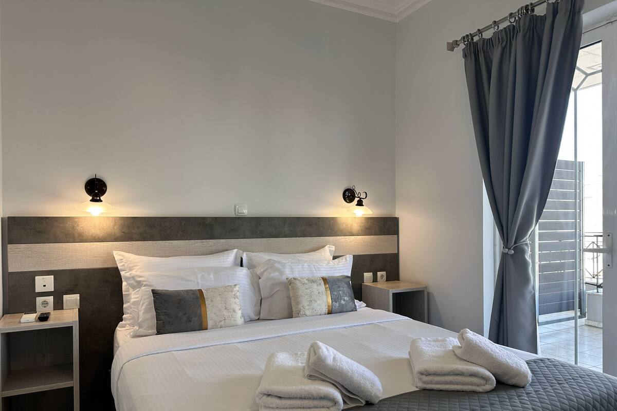 Ein modernes Hotelzimmer mit einem großen Bett, zwei Nachttischen, Wandleuchten und Blick ins Freie.