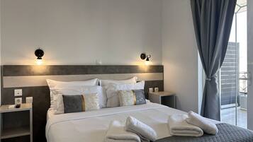 A modern hotel room with a large bed, two bedside tables, wall-mounted lights, and a view of the outdoors.