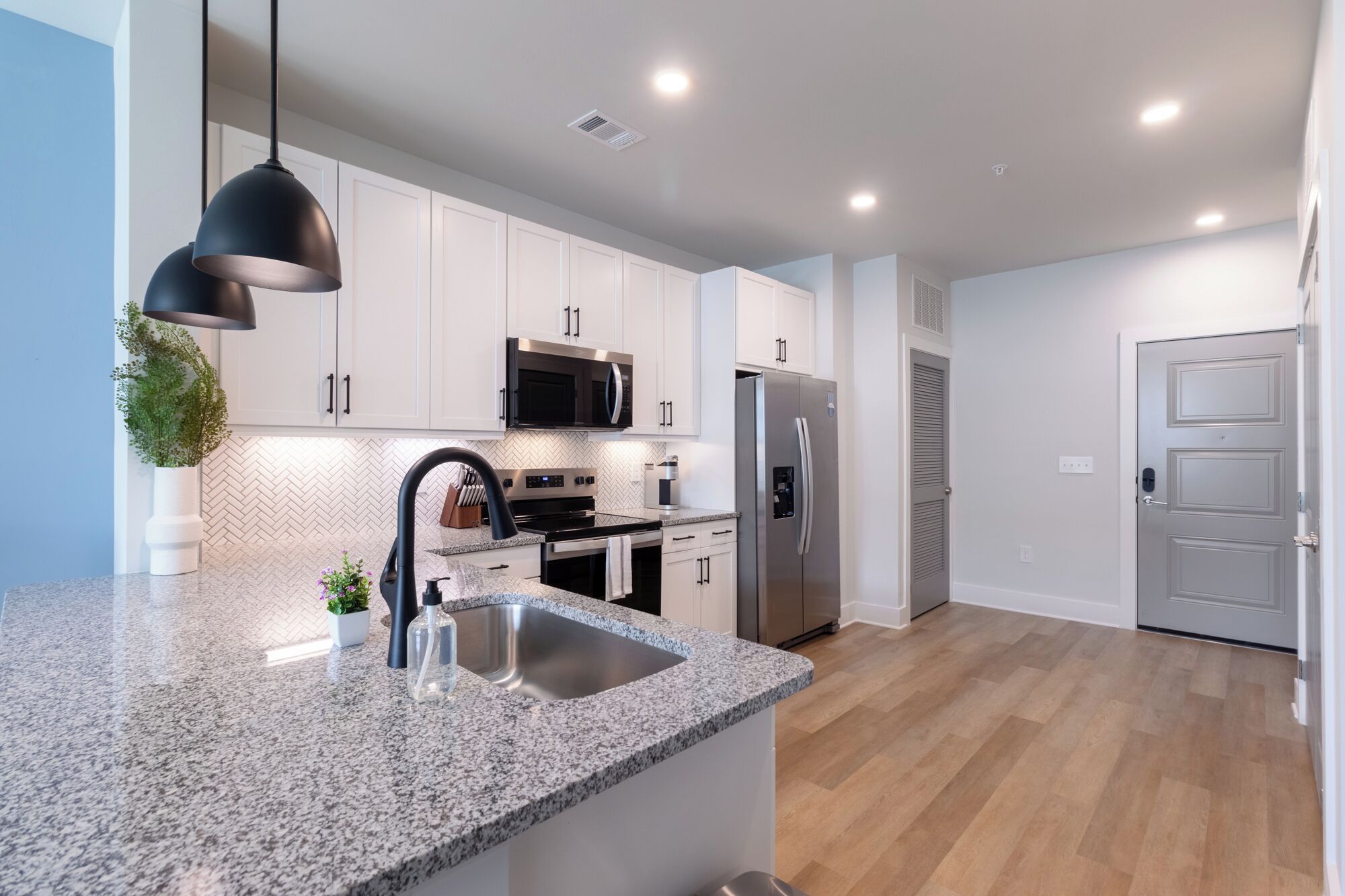 A modern kitchen with white cabinets, a granite countertop, stainless steel appliances, and pendant lighting.