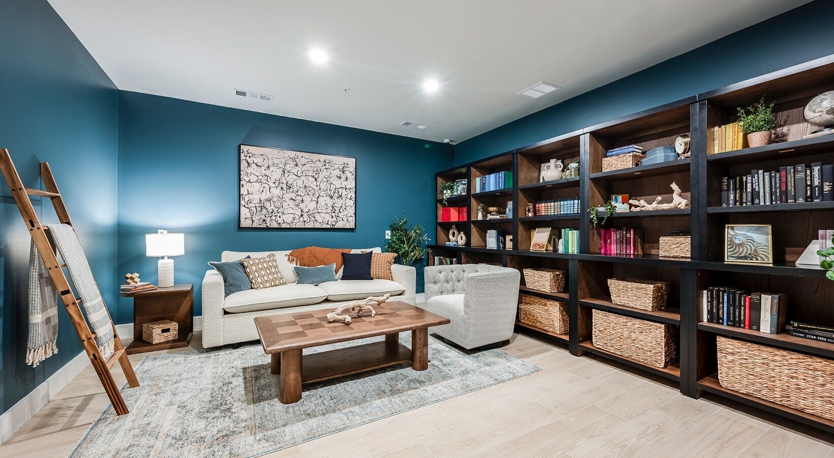 A living room with a sofa, armchair, coffee table, bookshelf, and a ladder leaning against the wall.