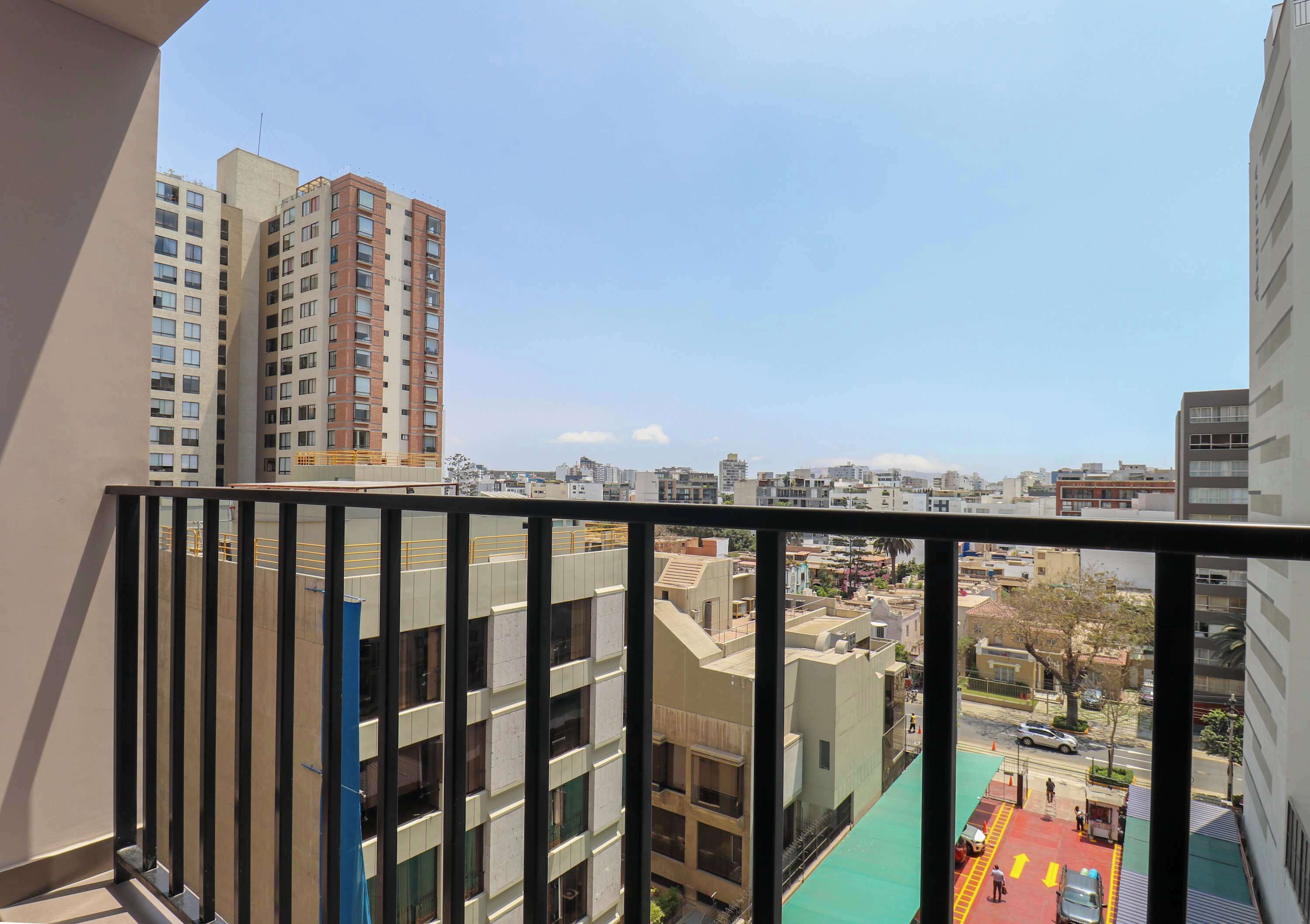 Ein Balkon mit Blick auf eine Stadtlandschaft, darunter hohe Gebäude und eine Straße mit Fahrzeugen.