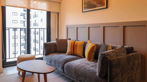 A modern living room with a grey sofa, a round wooden table, and a large window offering a view of a building. - w* | Marvelous 2BR with Balcony in Miraflores (Miraflores)