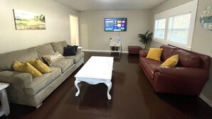 A living room with two sofas, a coffee table, a TV, and a clock on the wall. - The Magnolia / Cozy • Convenient • Urban • Vibrant (Birmingham)