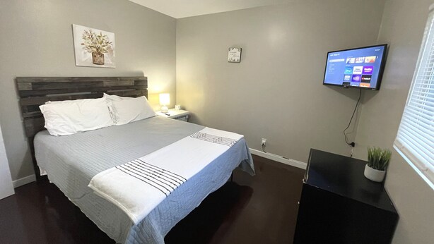 A hotel room with a bed, a nightstand, a TV mounted on the wall, and a small potted plant. - The Magnolia / Cozy • Convenient • Urban • Vibrant (Birmingham)