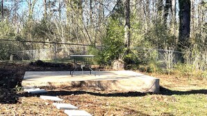 A concrete bench with metal legs in a wooded area with a metal fence in the background. - The Magnolia / Cozy • Convenient • Urban • Vibrant (Birmingham)