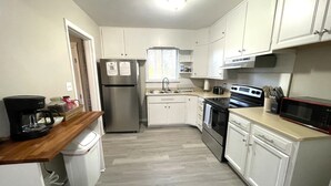 A compact kitchen with white cabinets, a stainless steel refrigerator, a microwave, and a coffee maker. - The Magnolia / Cozy • Convenient • Urban • Vibrant (Birmingham)