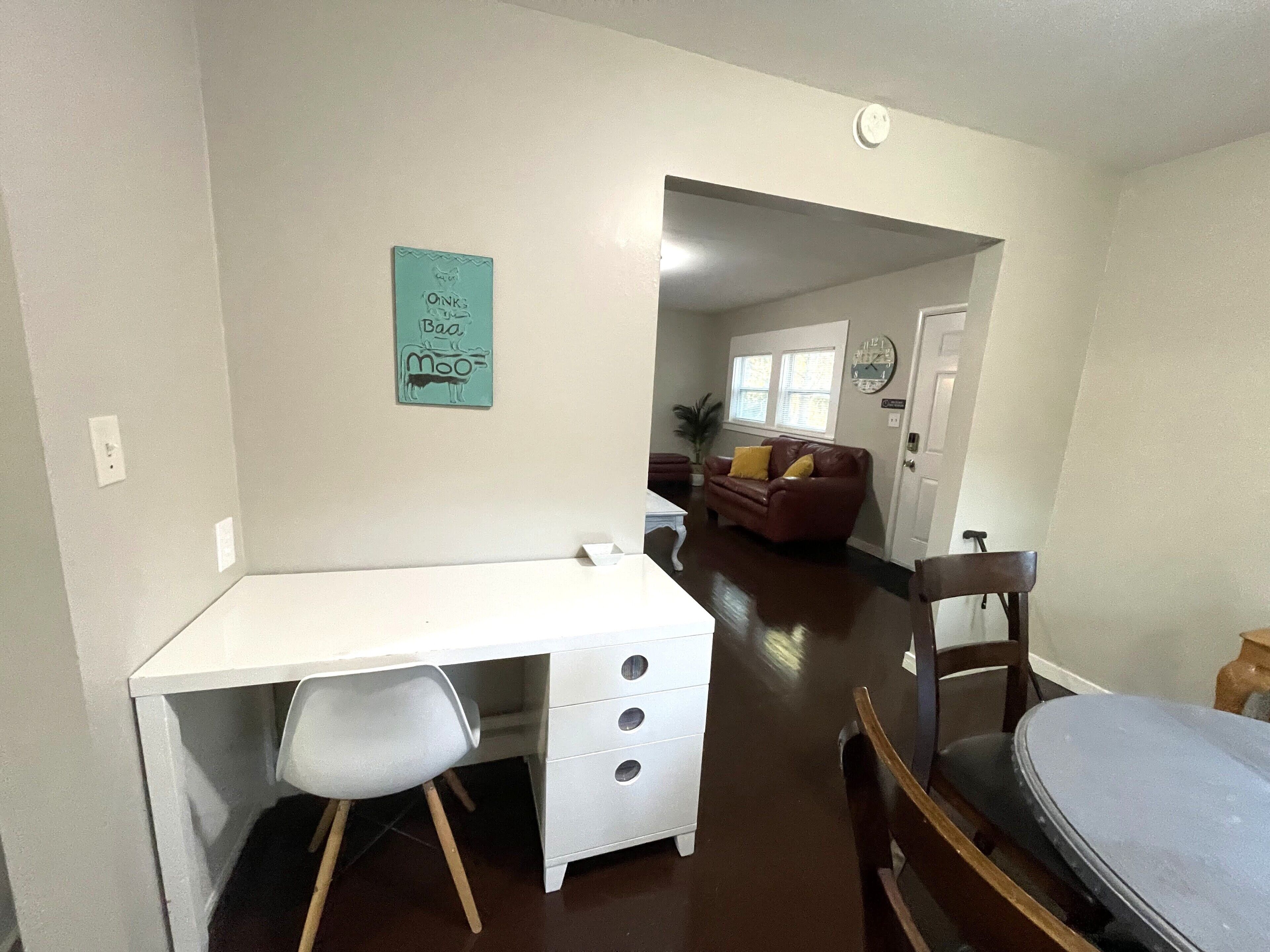 Un espacio habitable compacto con un escritorio blanco, una silla, un sofá de cuero marrón y una pequeña mesa.