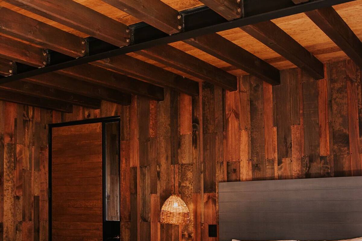 A bedroom with a wooden ceiling, a bed with white bedding, and a woven light fixture.