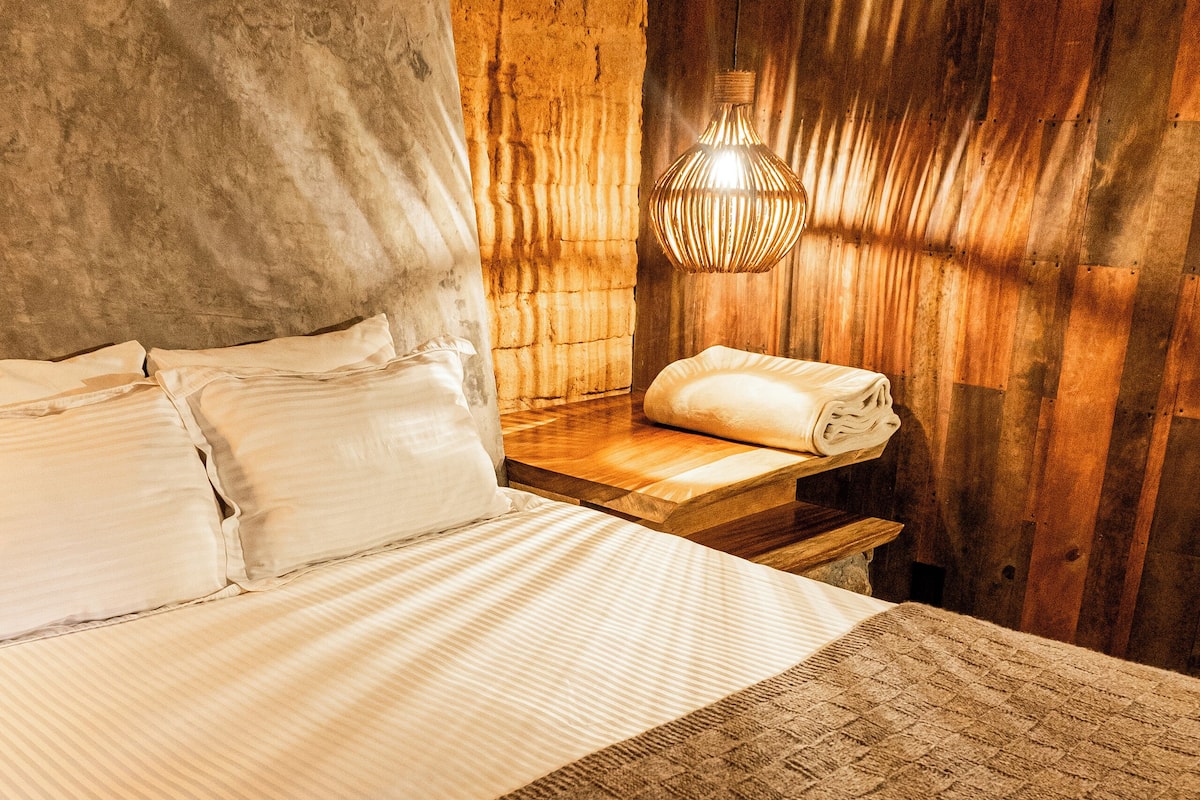 A neatly made bed with a striped blanket, a bedside lamp, and a folded towel on a wooden nightstand.