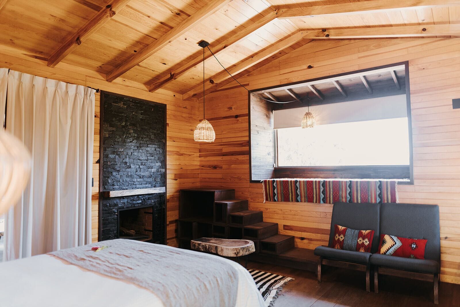 Una habitación acogedora con una cama, una chimenea, un banco y una ventana con vistas.
