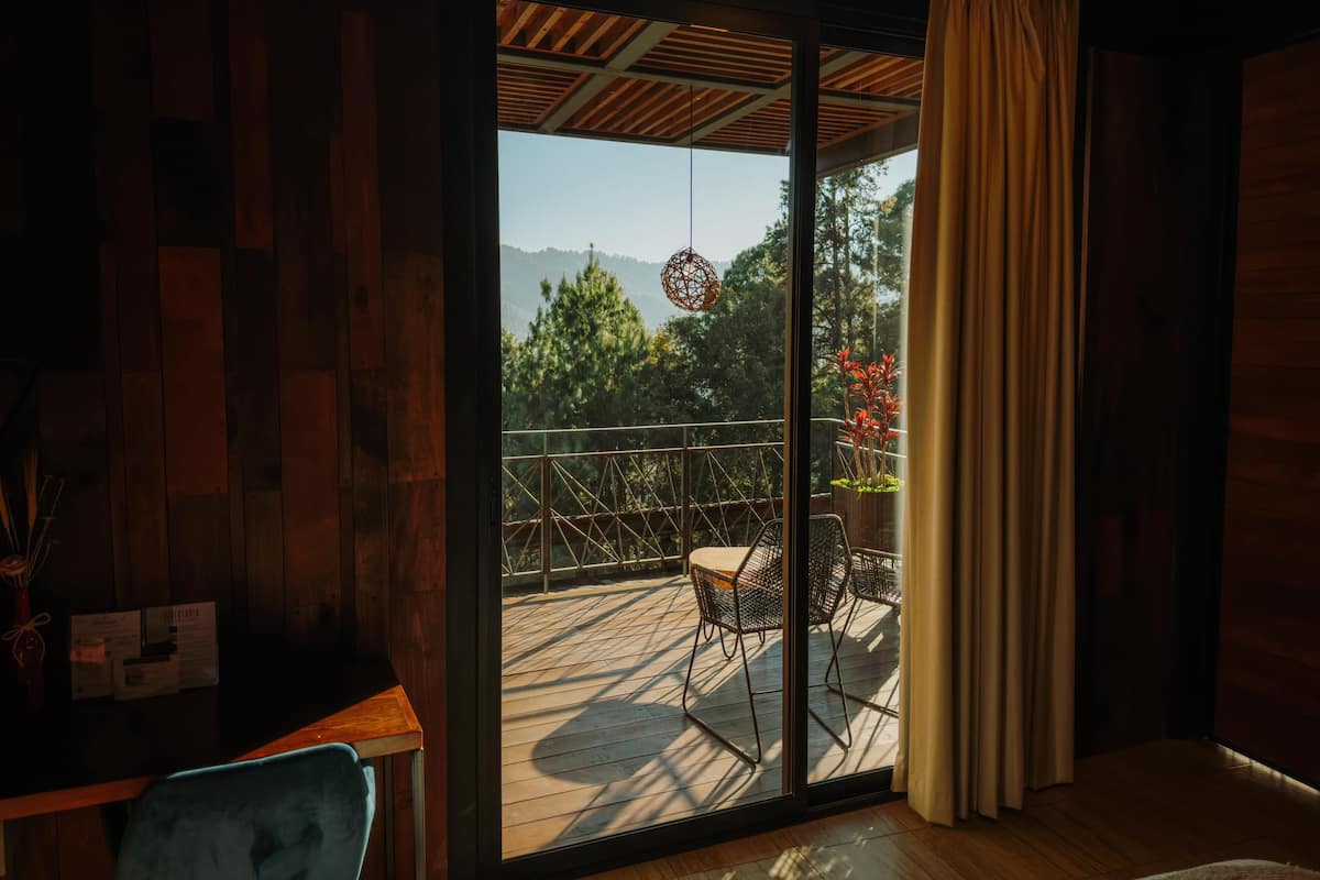 A room with a wooden floor, a sliding glass door leading to an outdoor deck with chairs and a hanging light fixture.