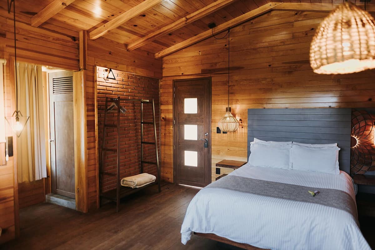 A wooden cabin bedroom with a bed, a bench, a ladder, and a door.
