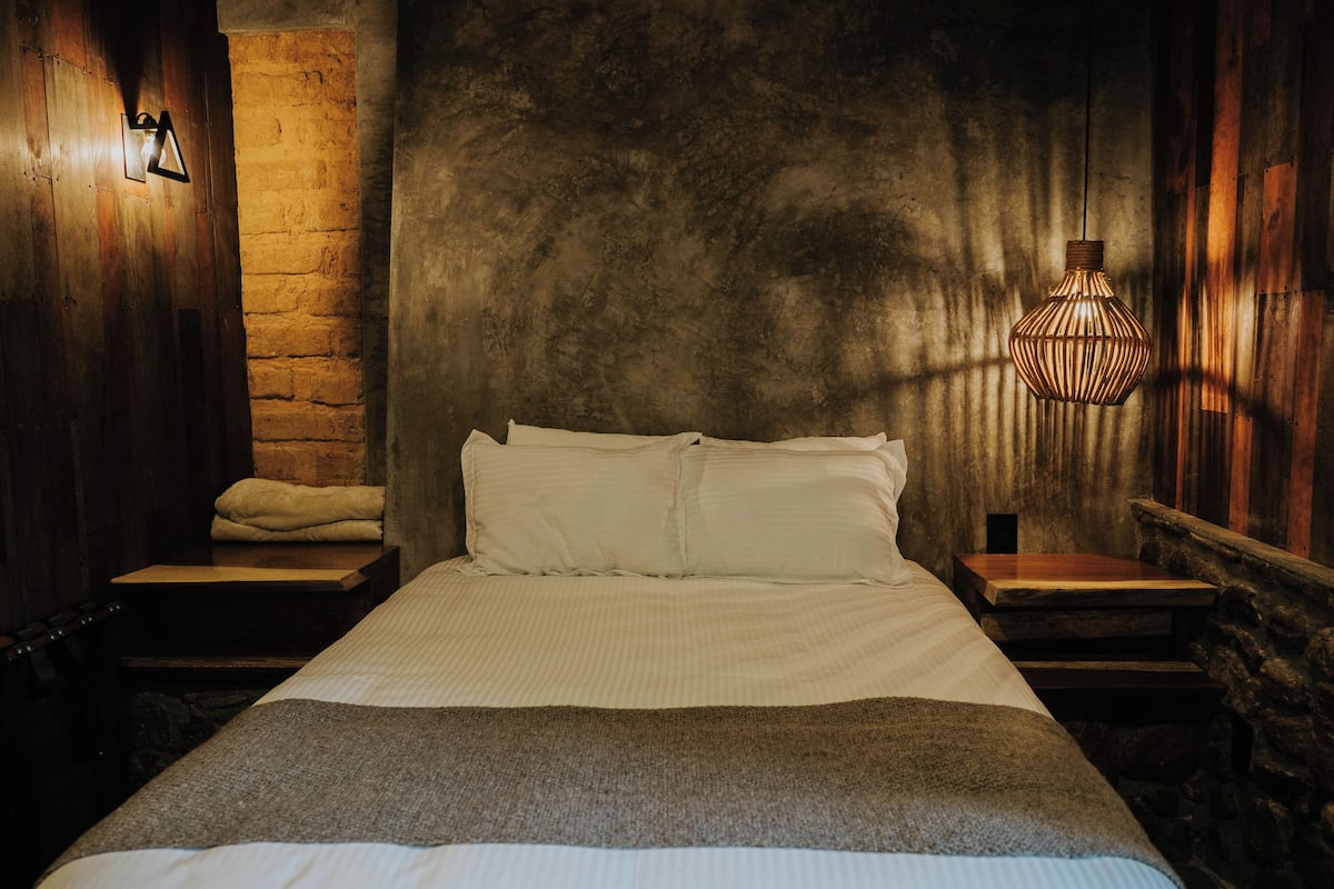 A room with a bed, two nightstands, a stone wall, and a hanging light fixture.