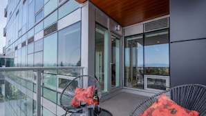 A balcony with glass railings, two wicker chairs with red cushions, a small round table, and a bottle of wine.