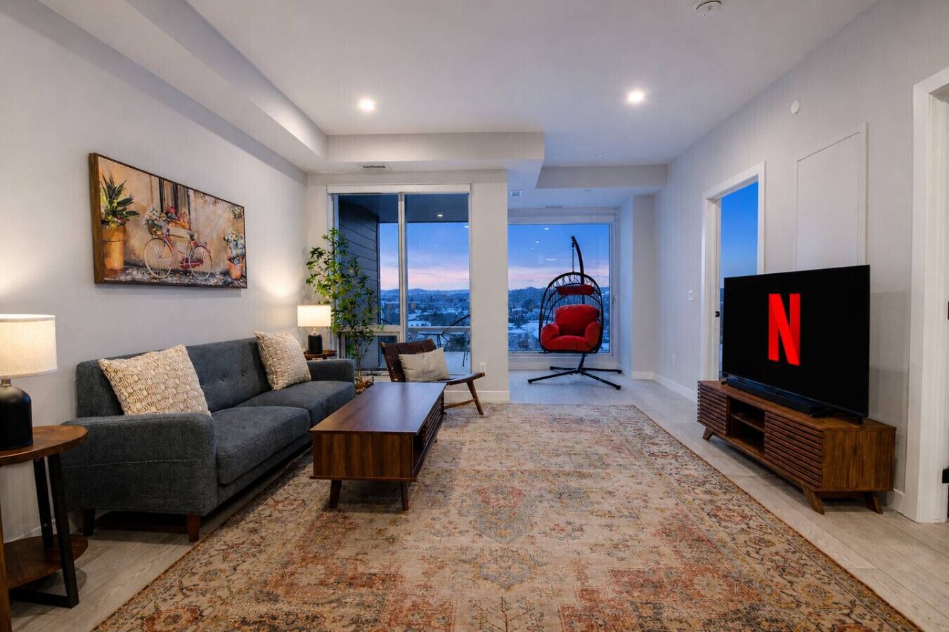 A modern living room with a sofa, coffee table, TV, and a large window with a view.