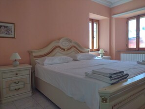 A neatly made bed with pillows and a folded towel, a bedside lamp, and a nightstand with drawers. - Casa Alta - 4 Bedroom Stunning Views and Villa with Pool in Medieval  Hill Town (Sant'Angelo in Pontano)