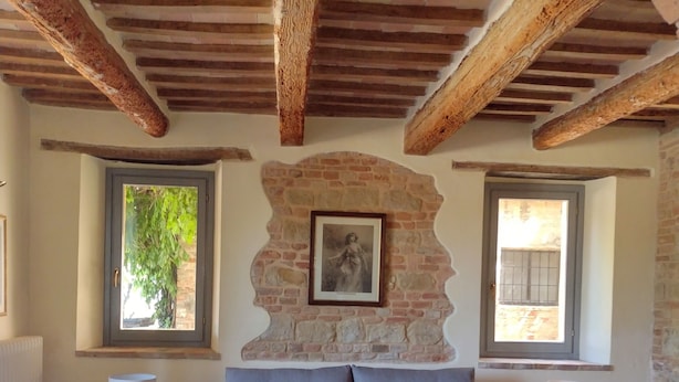 Un salón acogedor con un sofá gris, una mesa de centro de madera y dos mesitas auxiliares. Una pared de piedra con un marco de foto está detrás del sofá.