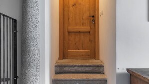A wooden door at the top of a staircase with stone steps and a stone column to the left. - Camera della Guardia - Pescate - Lecco (Lecco)