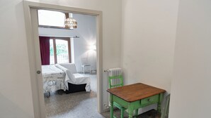 A room with a bed, a green chair, a wooden table, and a radiator. - Camera della Guardia - Pescate - Lecco (Lecco)