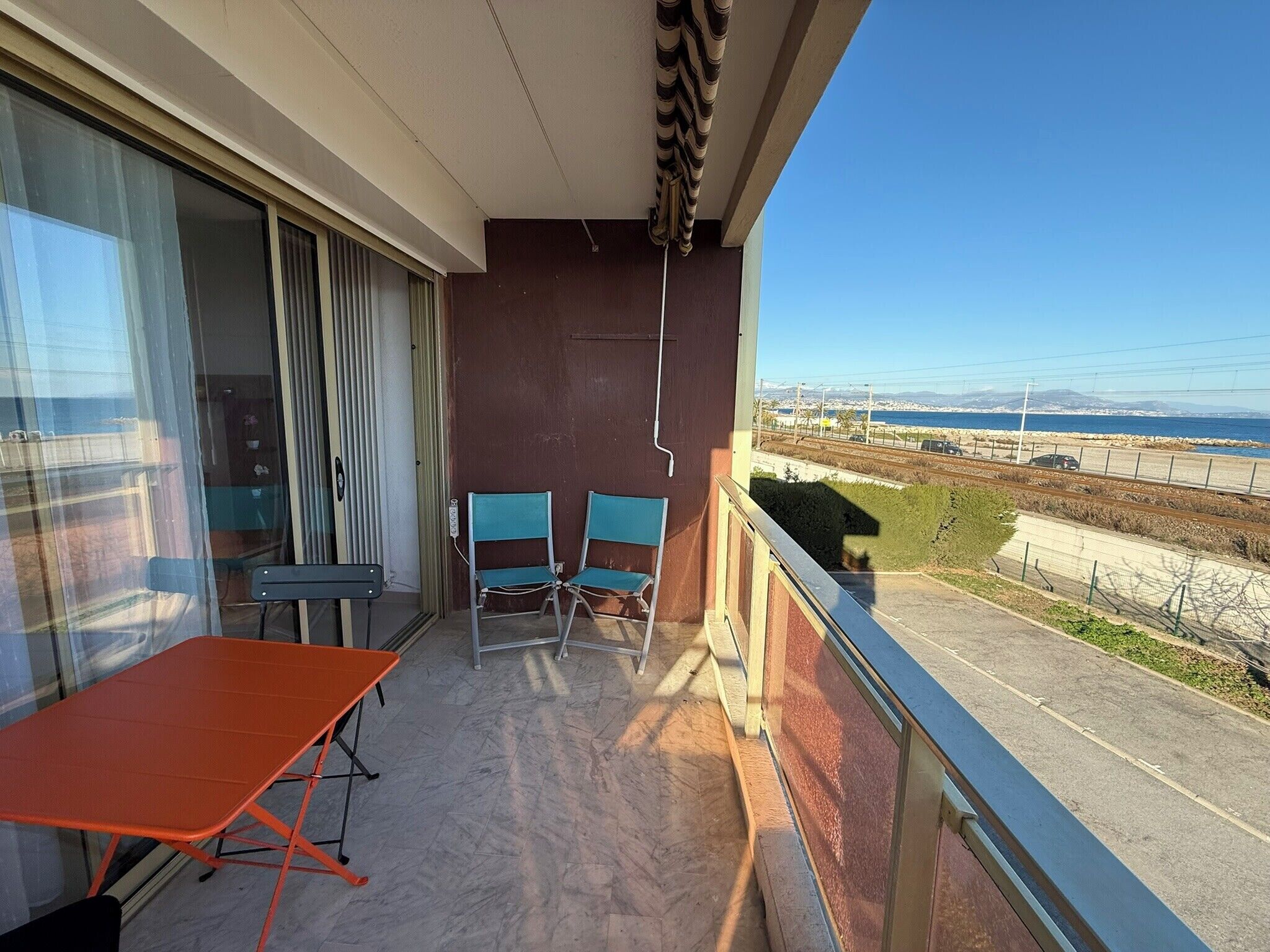 A balcony with a table and two chairs, a view of the sea and a railway track.