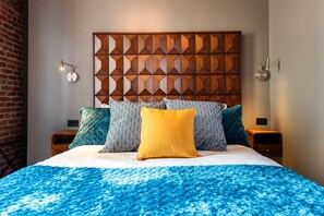 Une chambre d’hôtel avec un lit, une tête de lit à motifs géométriques et deux tables de chevet avec des lampes.