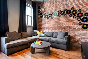 Una sala de estar con pared de ladrillo, un sofá modular, una mesa de centro y una estantería llena de discos de vinilo.