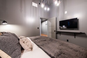 Une chambre à coucher moderne, avec un lit, un téléviseur fixé au mur et une porte donnant sur une autre pièce.