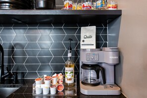 Zona cuina amb cafetera, ampolla de siroop de vainilla i diferents condiments al taulell.