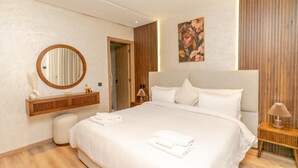 Moderni hotellihuone, jossa on suuri sänky, pyöreä peili, puinen meikkipöytä ja taulu seinällä.