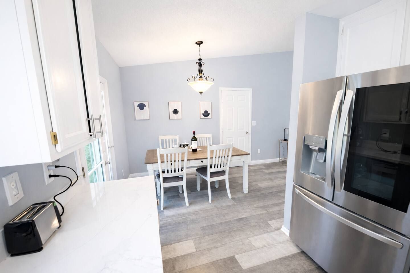 A modern kitchen with white cabinetry, a stainless steel refrigerator, and a dining area with a wooden table and white chairs.