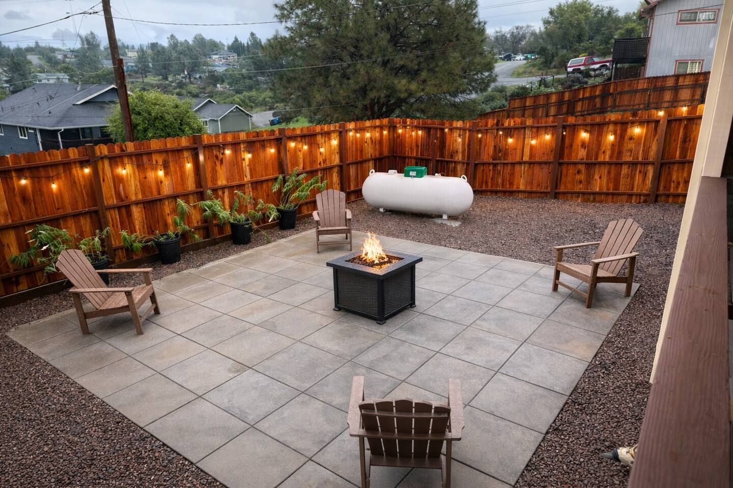 A patio with a fire pit, outdoor seating, a water feature, and a wooden fence with string lights.