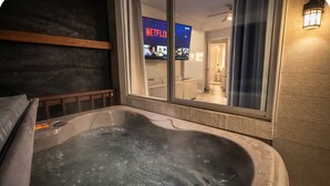 Un jacuzzi con vista a una habitación que tiene un televisor mostrando el logo de Netflix.