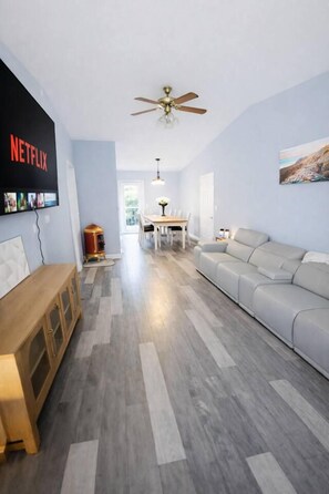 Sala de estar com sofá, um banco de madeira, ventilador de teto e TV na parede exibindo o logotipo da Netflix.