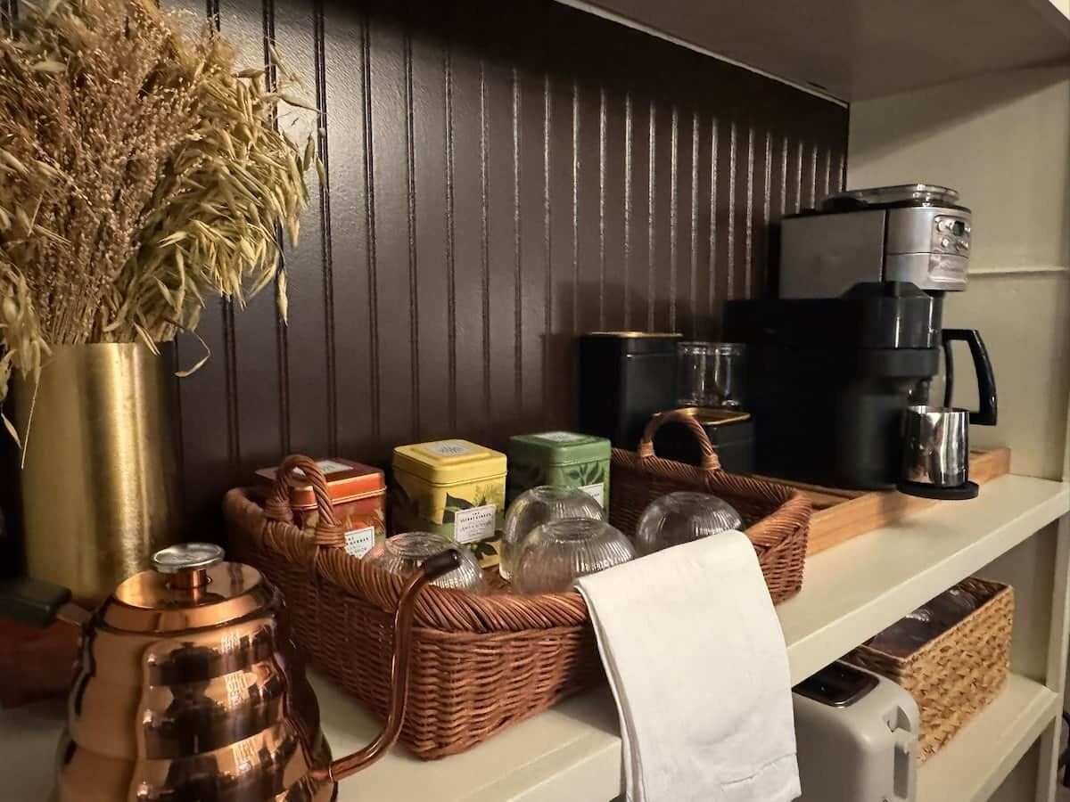 A kitchen counter with a coffee maker, wicker baskets, and a vase of dried flowers.