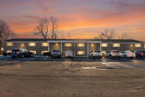 Ein Motel mit einer Reihe von Zimmern, einem Parkplatz und einem Sonnenuntergangshimmel.
