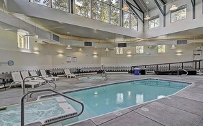 Un espace piscine doté de chaises longues, d’un jacuzzi et offrant une vue sur l’extérieur grâce à de grandes fenêtres.