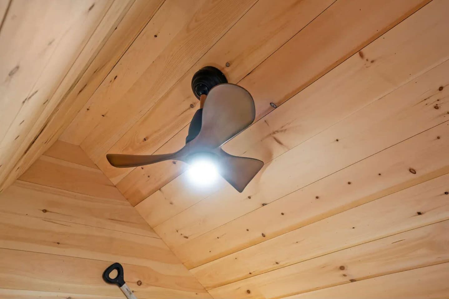 Un ventilador de techo en una habitación de madera con vigas a la vista y una lámpara.