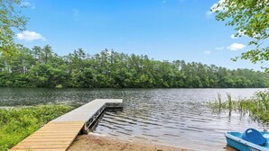 A wooden dock extending into a lake surrounded by dense trees.