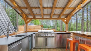 An outdoor kitchen with a stainless steel grill, a sink, and wooden deck flooring.
