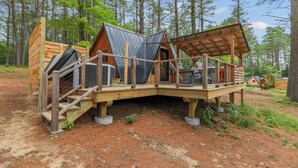 A cabin with a wooden deck, a covered outdoor seating area, and a staircase leading to the entrance.
