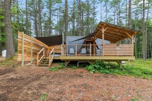 A wooden cabin with a deck, a covered area, and a staircase leading to a loft.