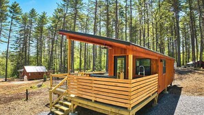 A wooden cabin with a deck and a small porch, surrounded by a forest. - Modern Glamping Cabin with Hot tub (Oxford)