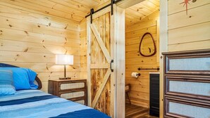 Una habitación con piso y muebles de madera, que incluye una cama, una mesita de noche, una lámpara, una puerta de madera y un espejo.